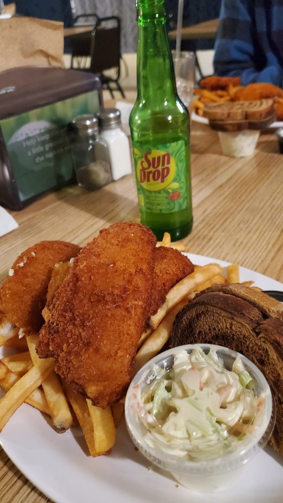 A Wisconsin Friday night fish fry with breaded fish, fries, coleslaw, rye bread, and a bottle of Sun Drop at a small-town bar.